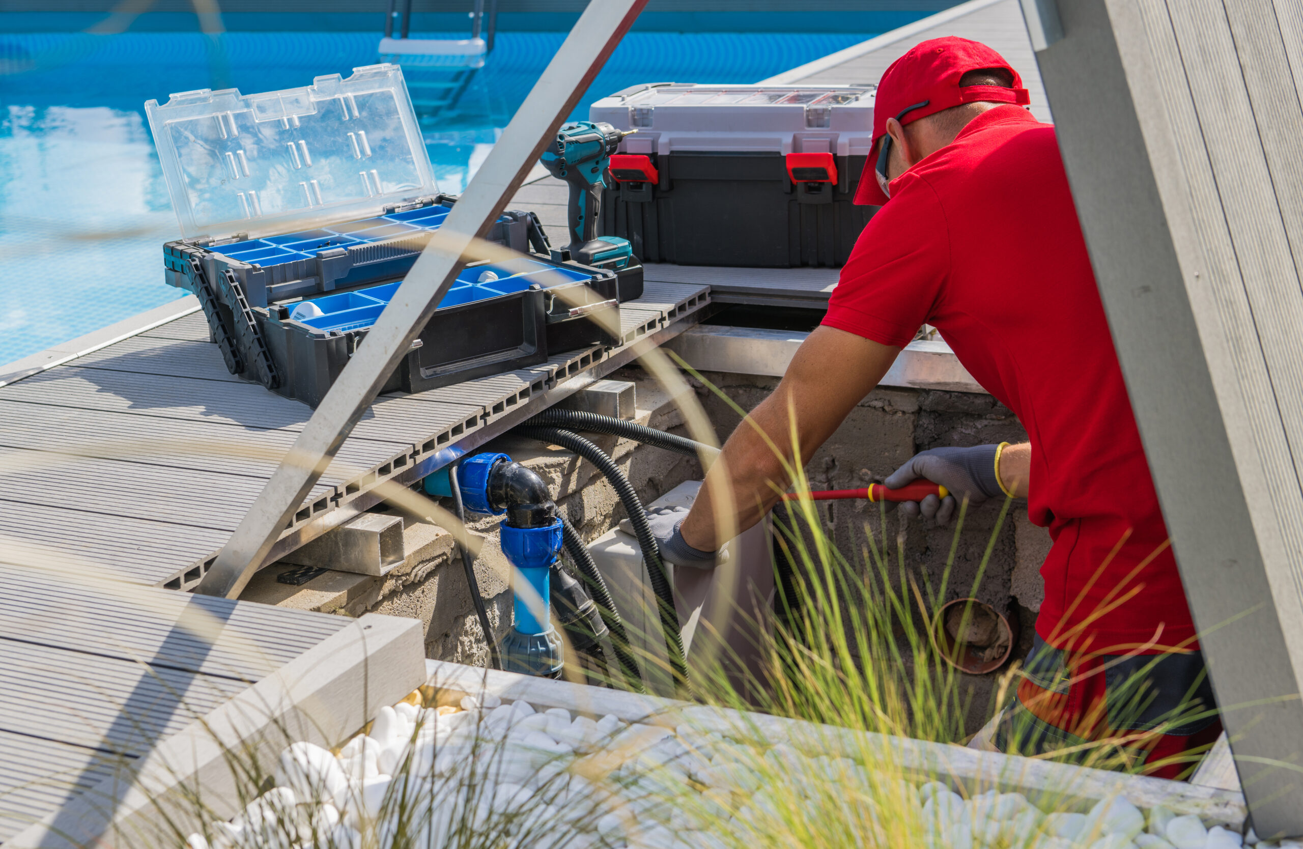 Closeup of Caucasian Professional Worker in Red Uniform Fixing Outdoor Swimming Pool Heating System Using Different Tools. Side View.